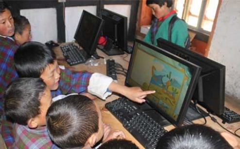 A small group of children is gathered around a computer, with one child pointing at the screen displaying a colorful cartoon. This scene represents children engaging with educational technology.