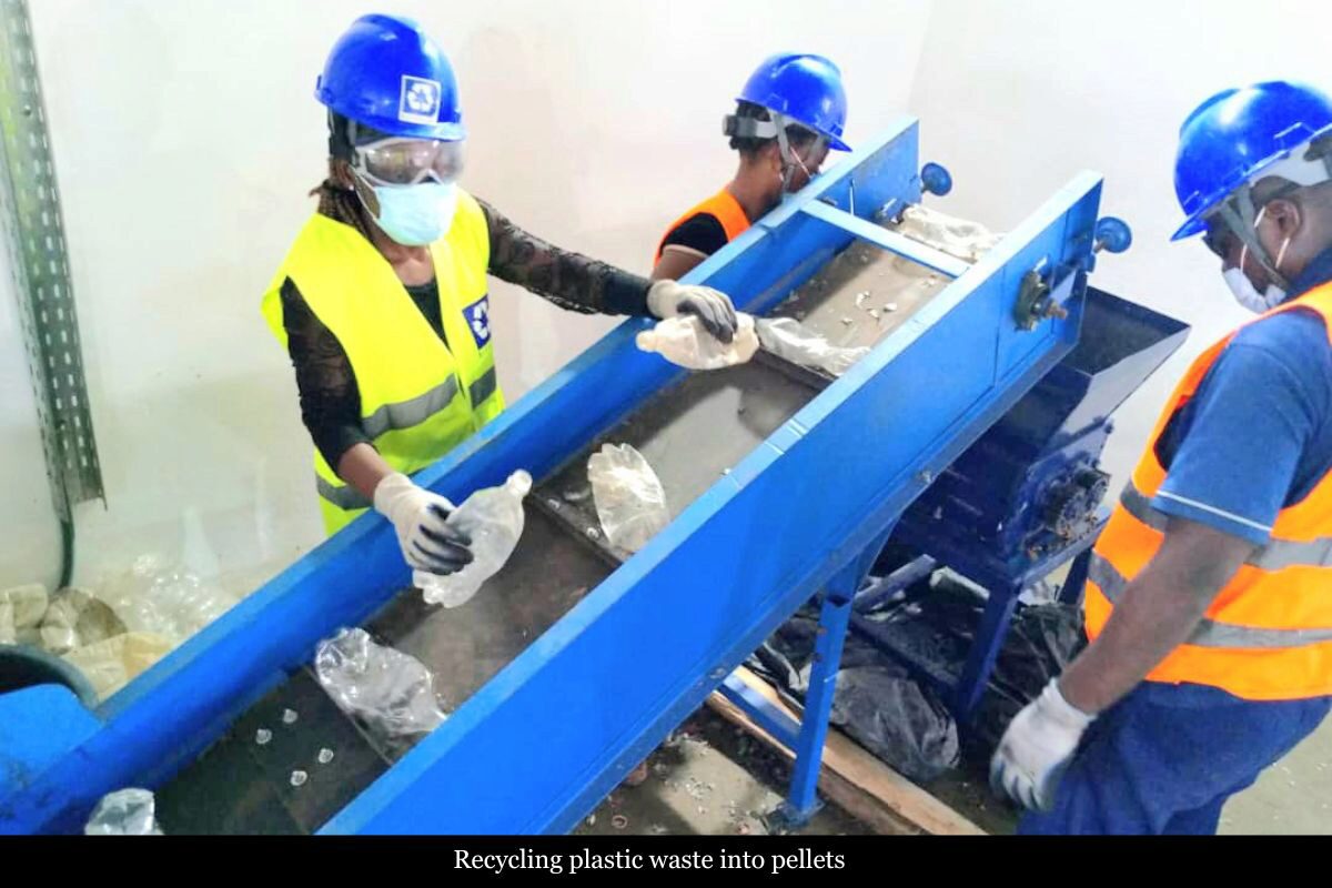 Workers wearing protective gear operate a recycling machine, sorting plastic waste on a conveyor belt.