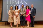 A small group of people standing together, dressed in formal attire. Behind them, there is a backdrop with the words "Lipman Family Awards".