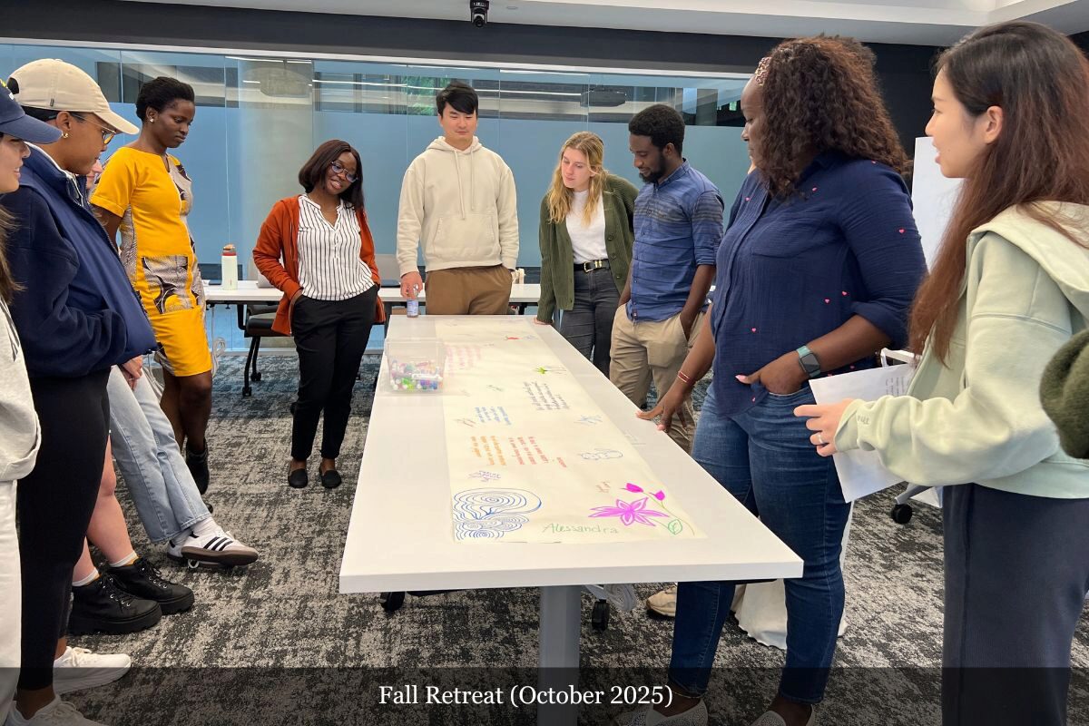 A small group of people in casual attire standing around a table with paper, decorations, and drawings. The setting appears to be a workshop or brainstorming session.