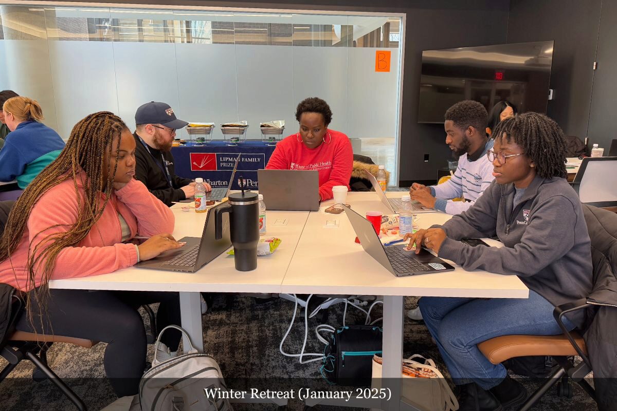 A small group of people engaged in a collaborative work session at a table with laptops and beverages, in a conference room setting.