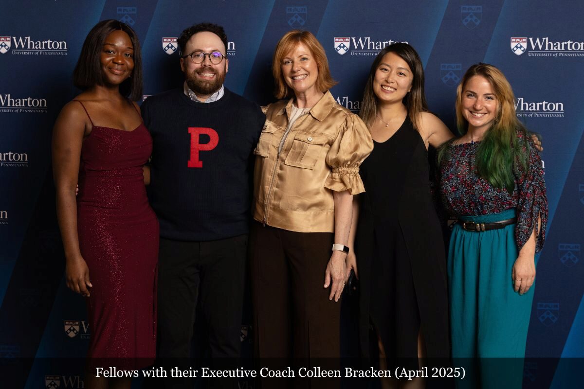 A small group of people posing in front of a Wharton University of Pennsylvania backdrop. They appear dressed for a formal or professional event.