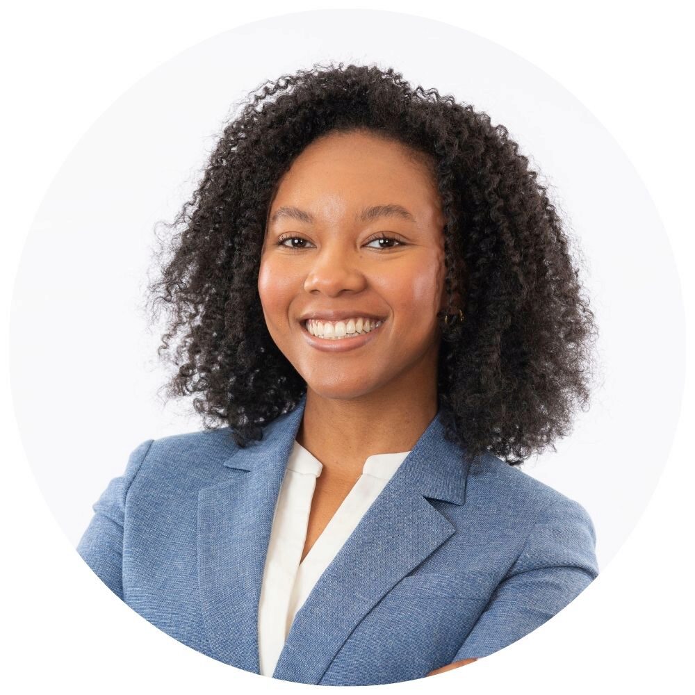 Lauryn McSpadden Headshot of a person with curly hair, wearing a blue blazer over a white blouse, smiling at the camera.