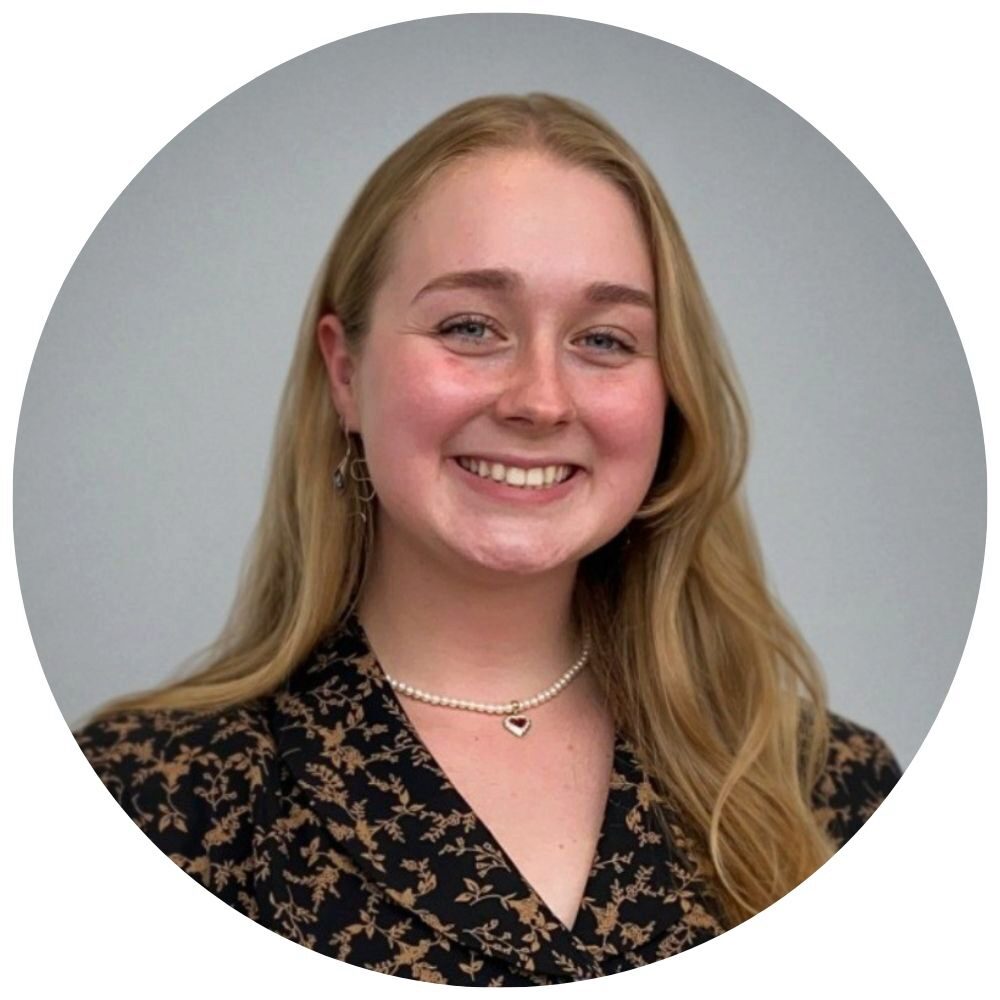 Fionnuir Ni Chochlain Headshot of a smiling person with long blond hair wearing a patterned top and jewelry.